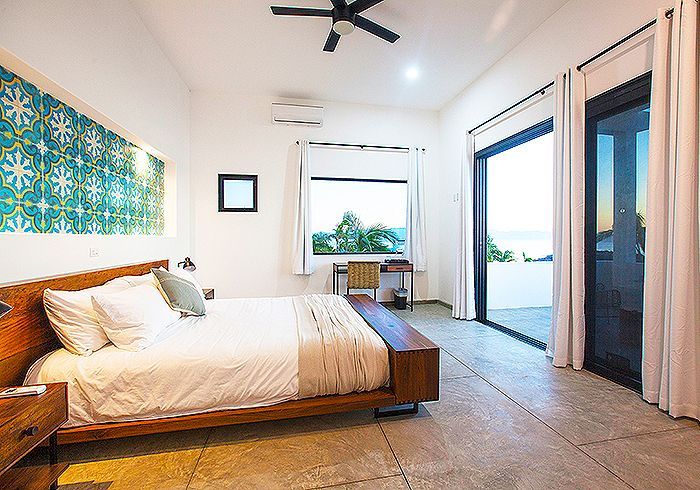 Bedroom with bed, patterned wall decor, and large sliding doors to a patio overlooking the ocean.