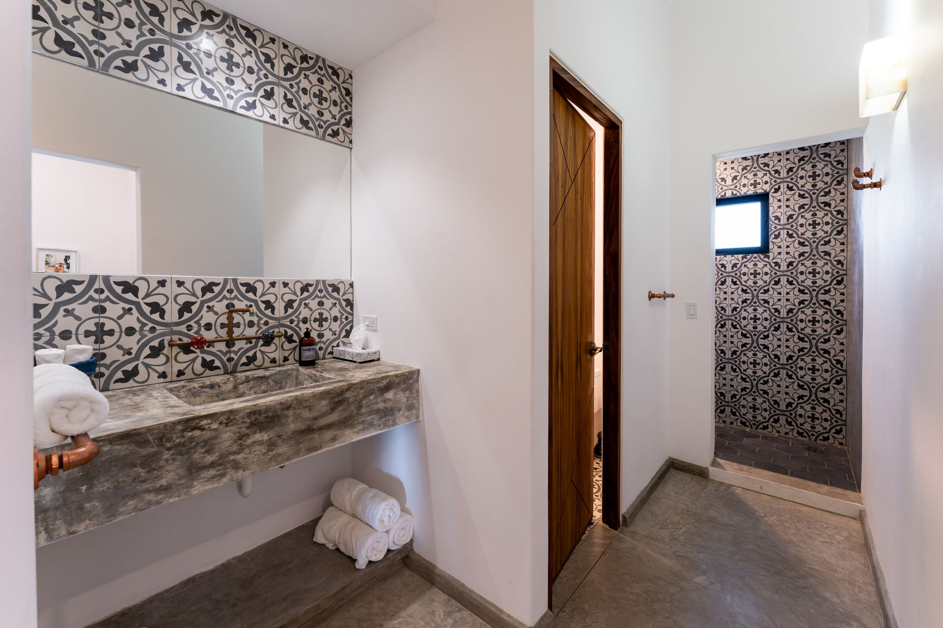 Bathroom with patterned tiles, concrete sink, white walls, and wooden door.