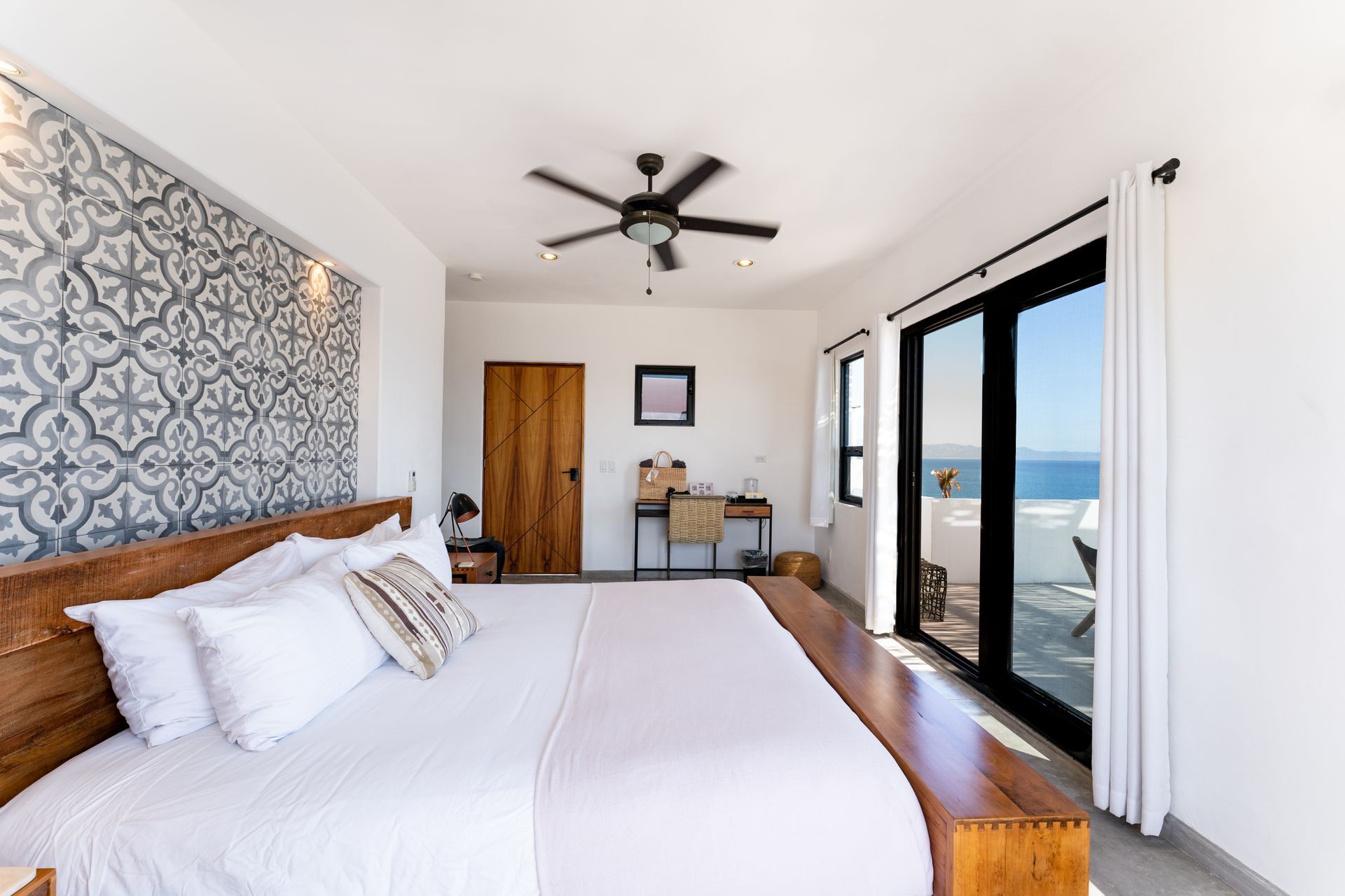 Bedroom with ocean view; king bed, patterned accent wall, desk, sliding glass doors, and ceiling fan.