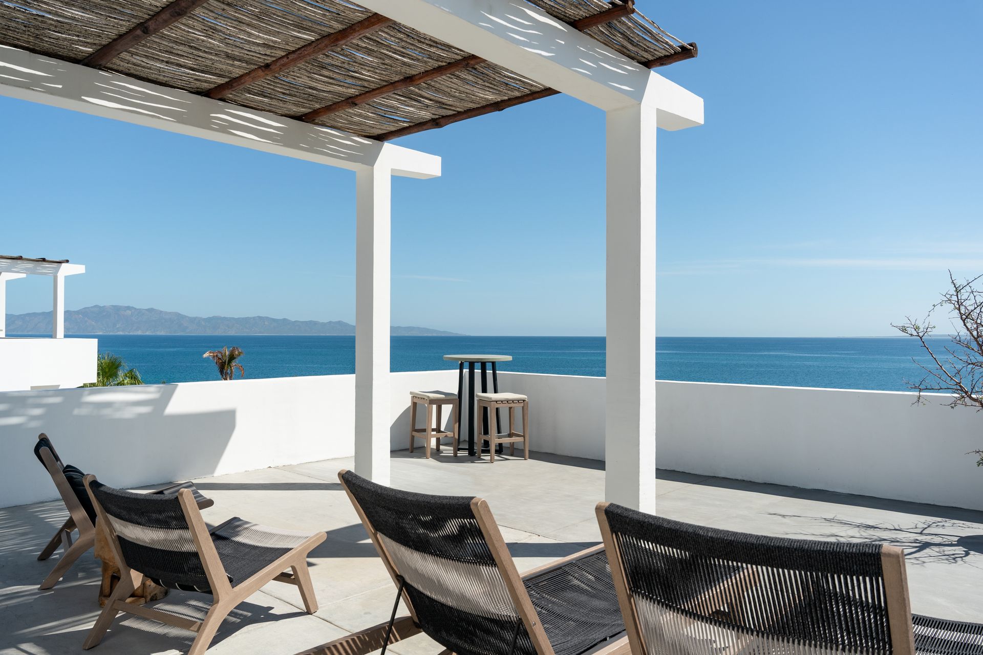 Terrace with white pillars, woven roof, ocean view, chairs, and table.