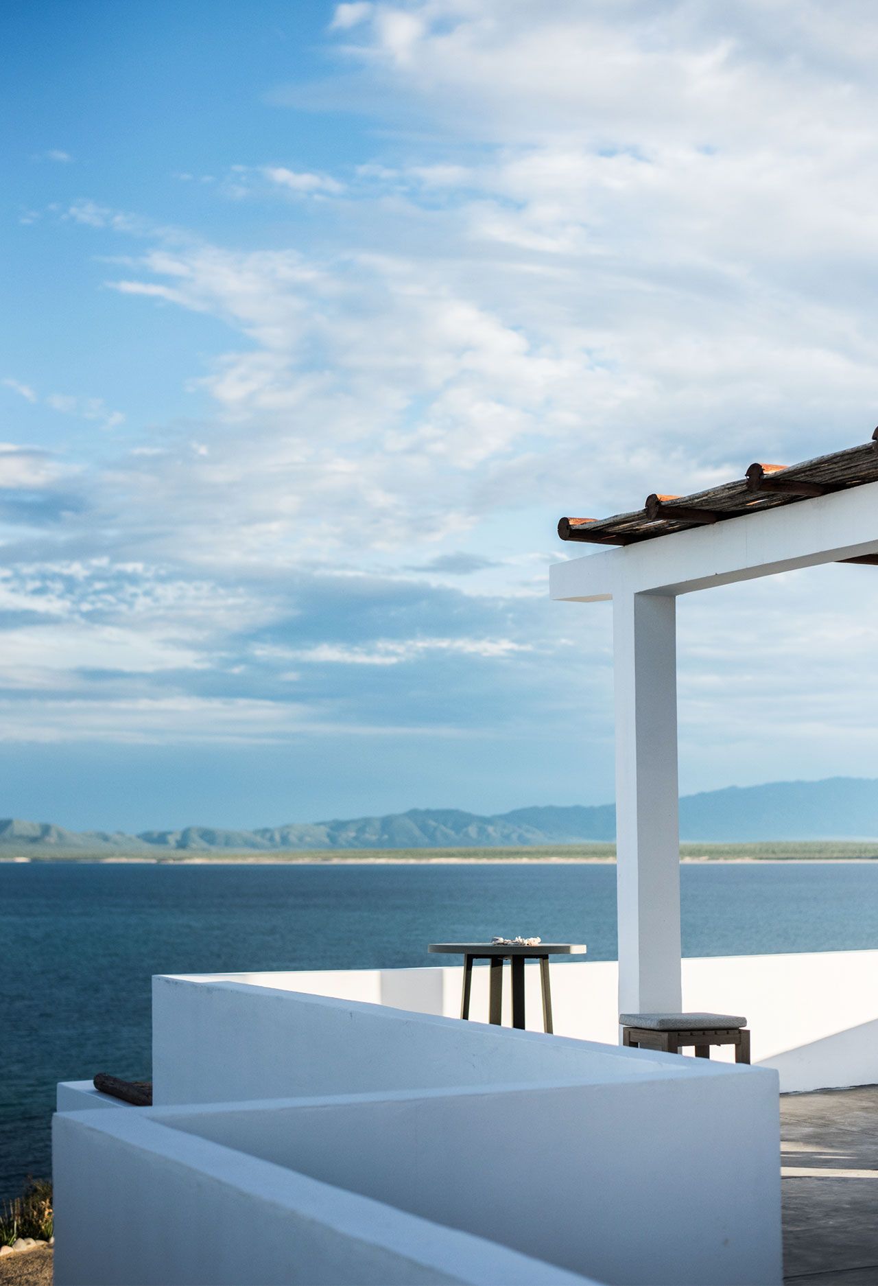 White balcony overlooking blue ocean and distant mountains under a cloudy sky.