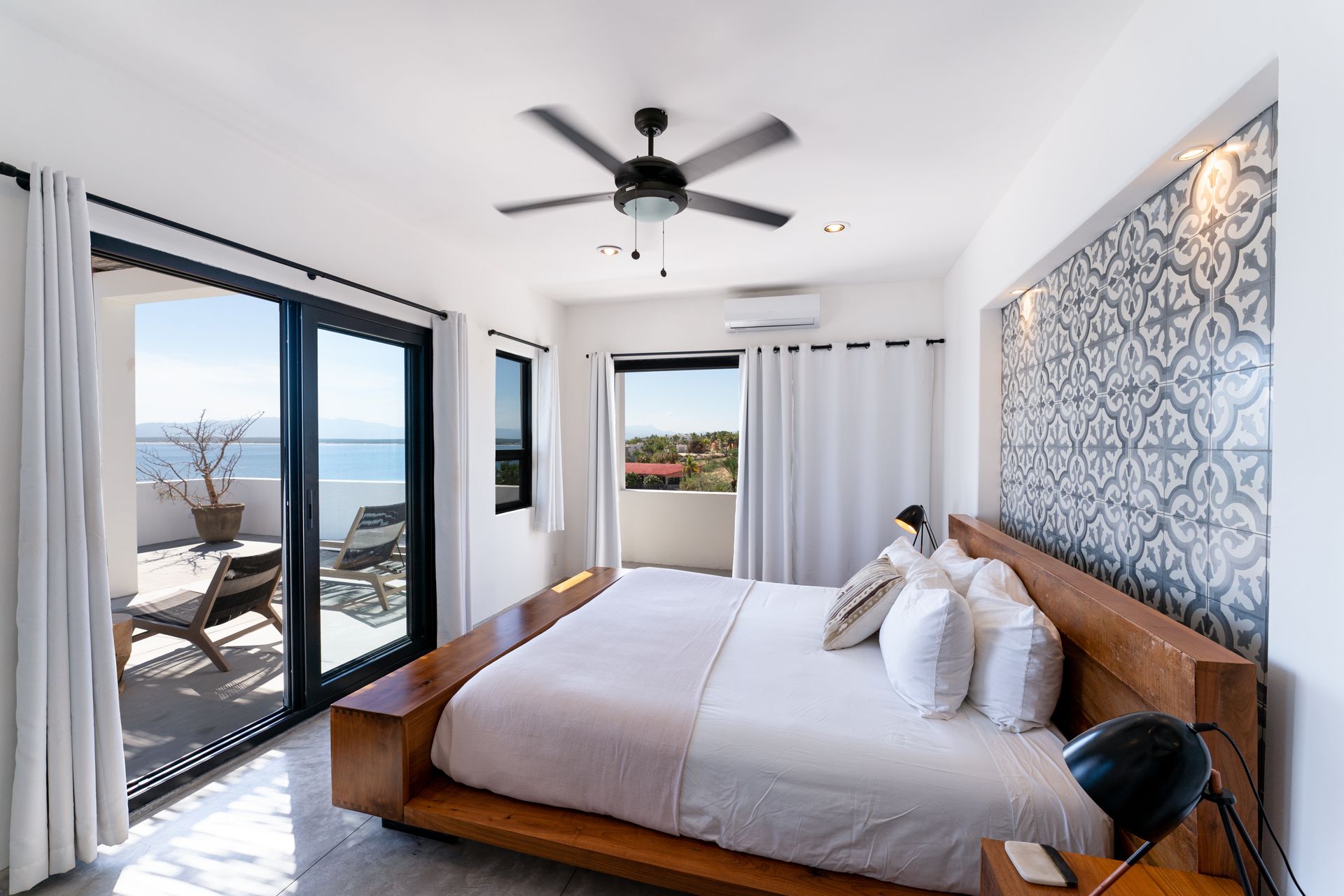 Bedroom with bed, balcony with ocean view, black ceiling fan, and patterned wall.
