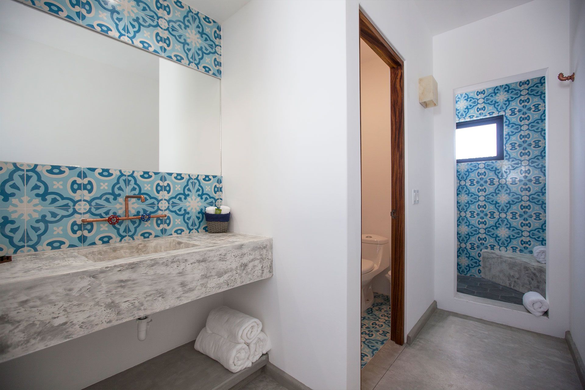 Bathroom with patterned blue tile, stone countertop, open doorway to toilet, concrete floor.