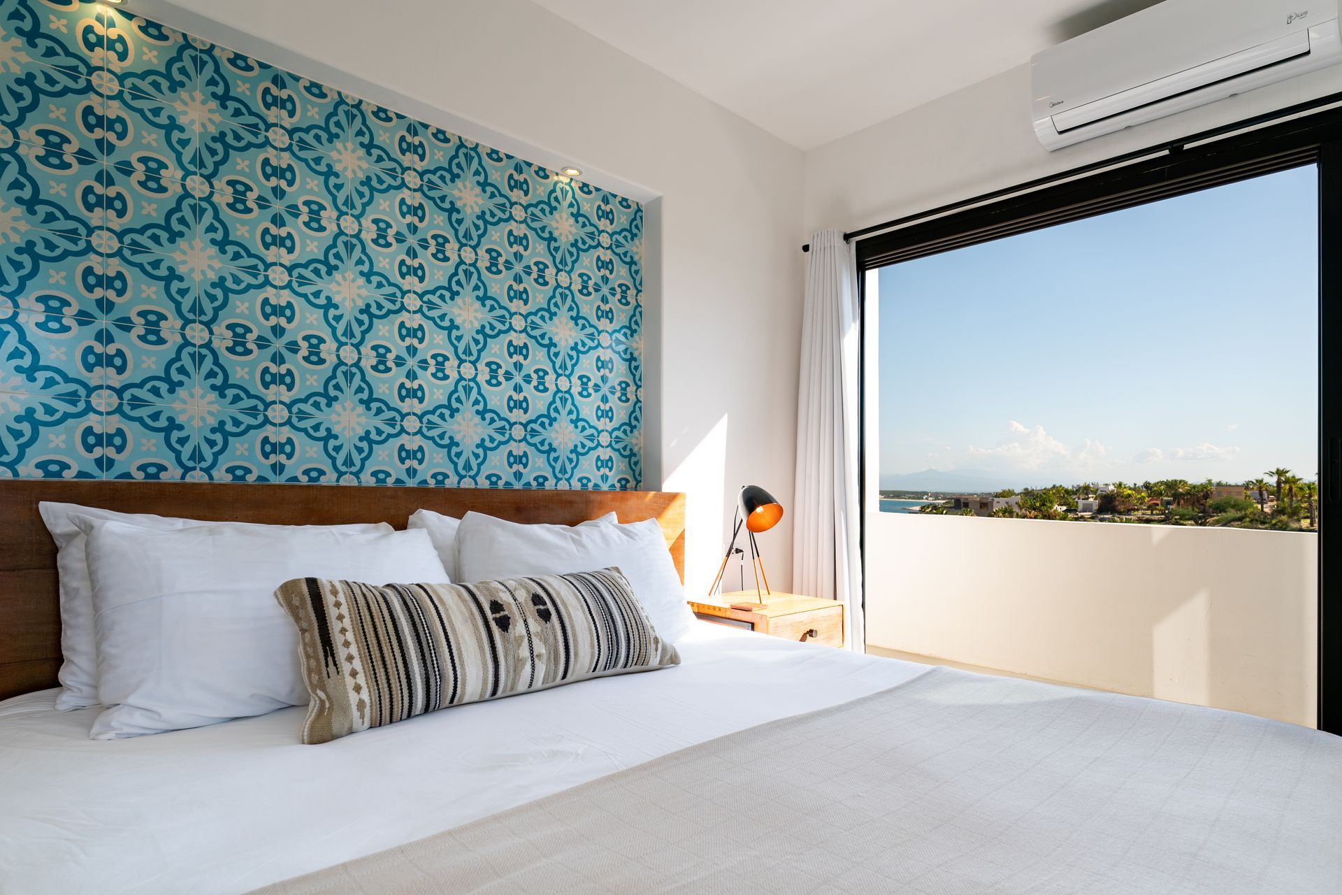 Bedroom with blue patterned accent wall, bed, and open glass doors overlooking a sunny view.