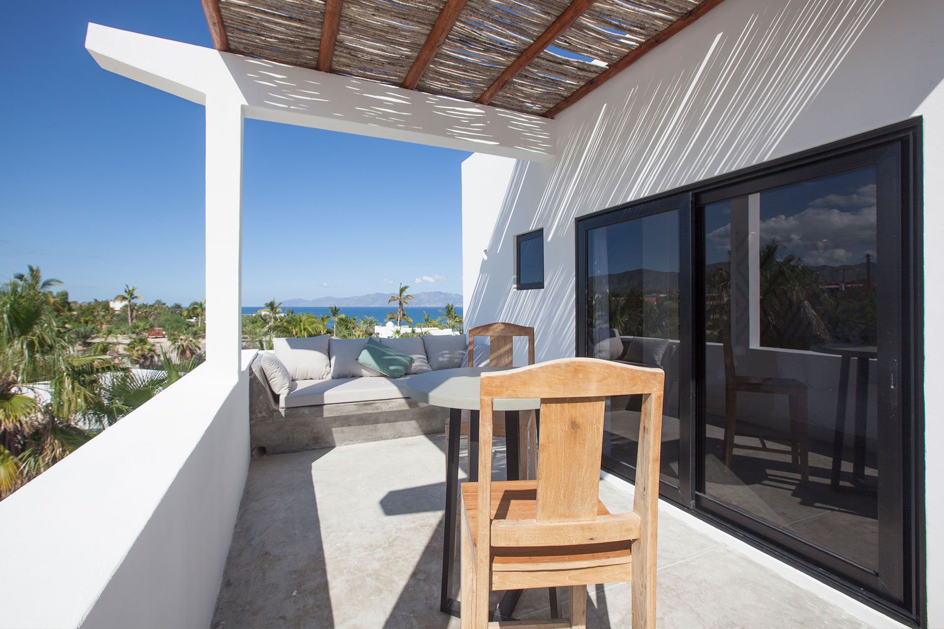 Balcony with seating, ocean view, bright blue sky.