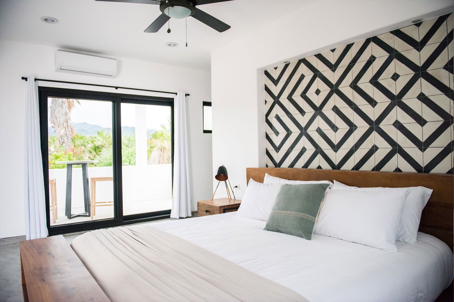 Bedroom with a large bed, wooden furniture, geometric headboard, and sliding glass doors to a balcony.