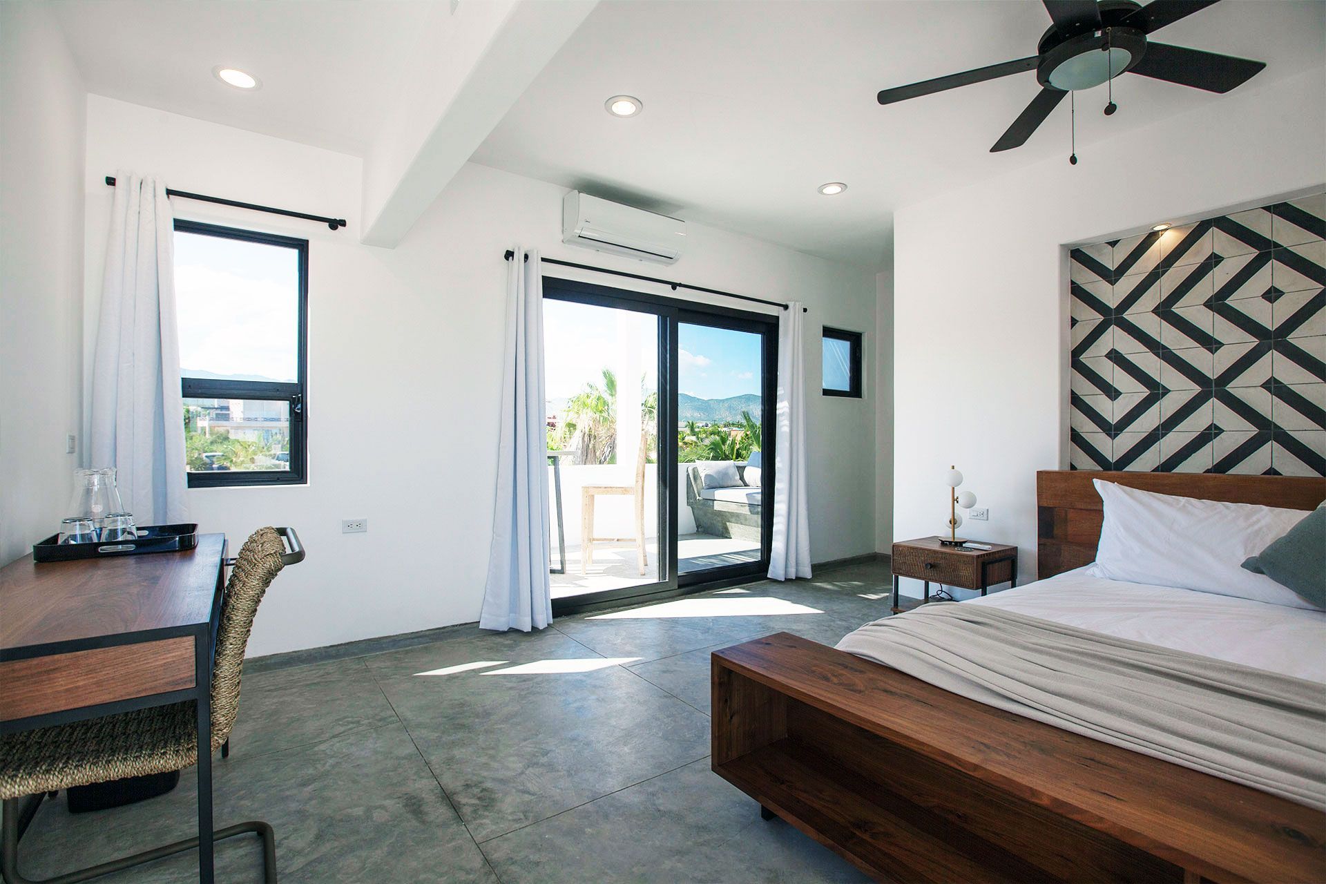 Modern bedroom with large windows, balcony access, wooden bed, and desk.