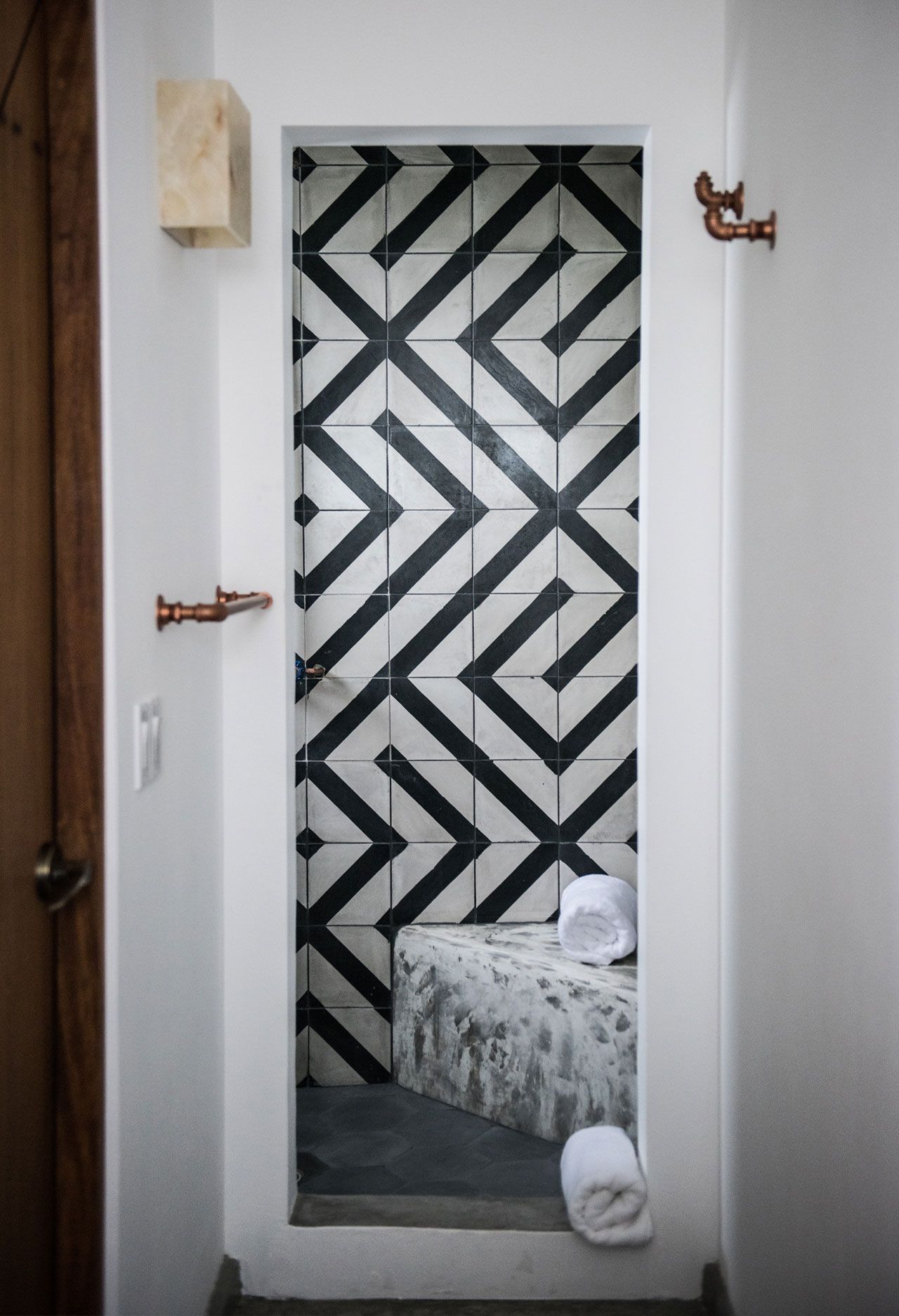 Bathroom alcove with black and white geometric tile, concrete bench, and copper fixtures.