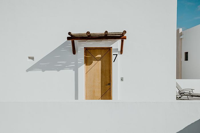 White building with wooden door, number 7, and small canopy casting a shadow.