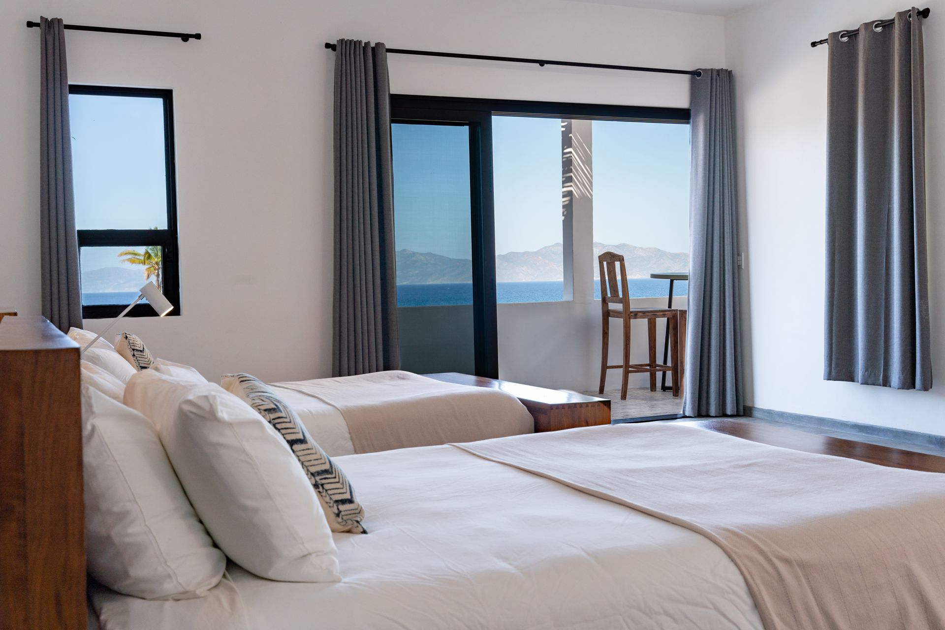 Bedroom with two beds facing a sliding glass door and an ocean view, gray curtains.