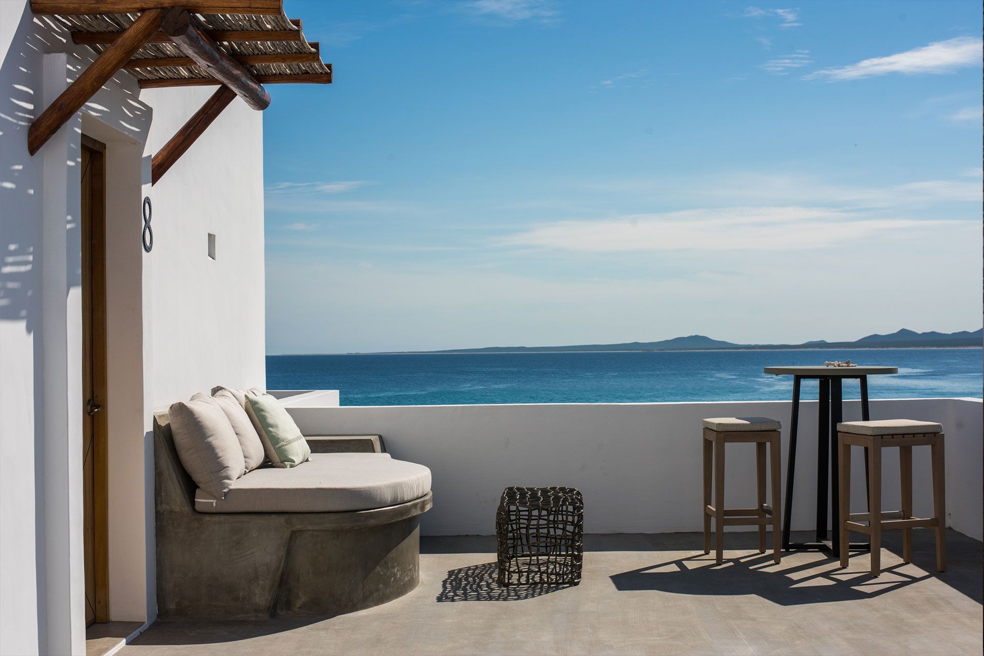 Terrace with built-in seating, stools, and ocean view on a sunny day.