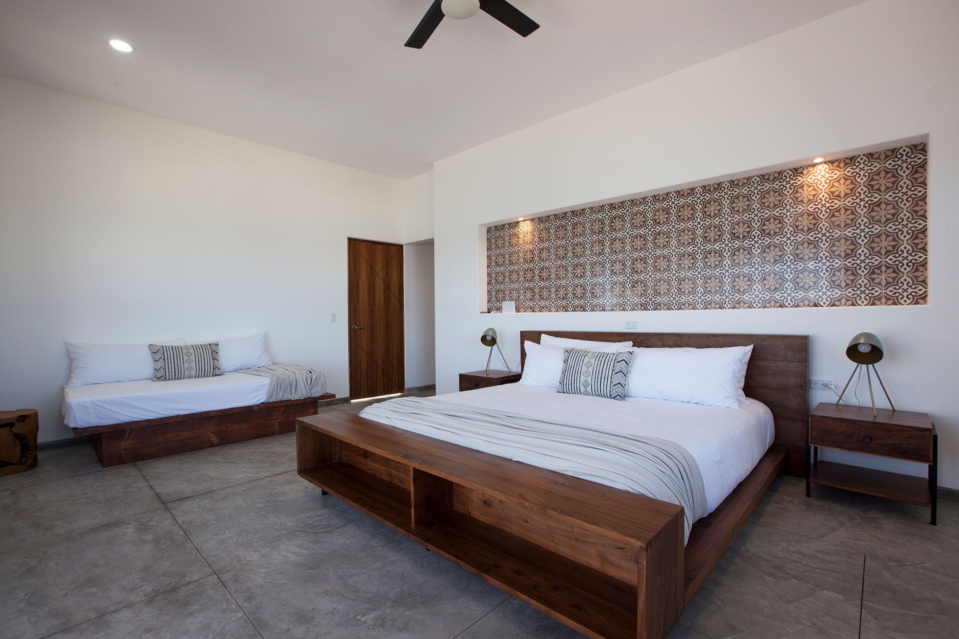Spacious modern bedroom with a wooden bed frame, sofa, and patterned wall decor, under a ceiling fan.