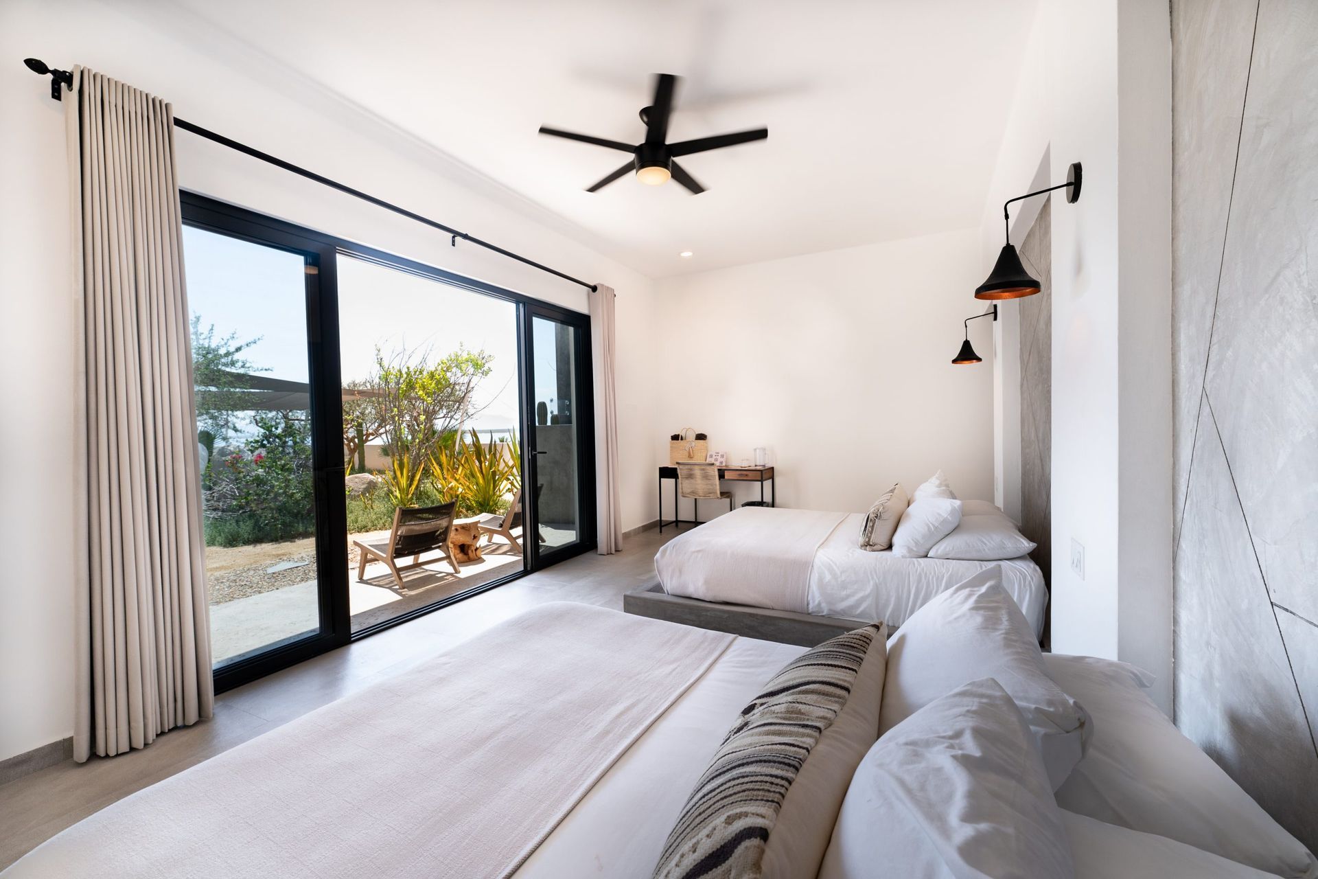 Bright bedroom with three beds, a patio door, desk, and black ceiling fan.