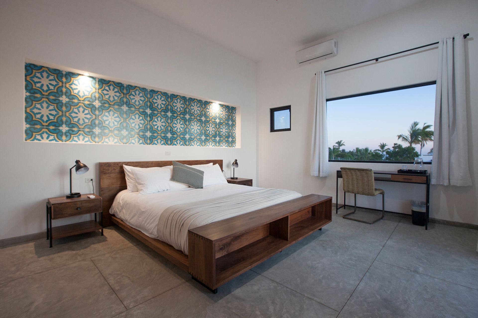 Modern bedroom with a large wooden bed, desk, and decorative tile wall.