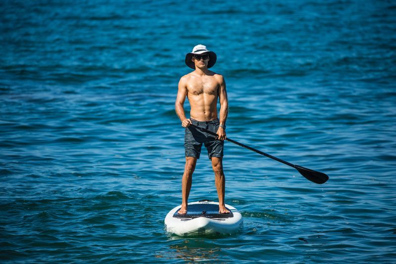 Man paddleboarding in ocean, wearing sunglasses and hat, holding a paddle.