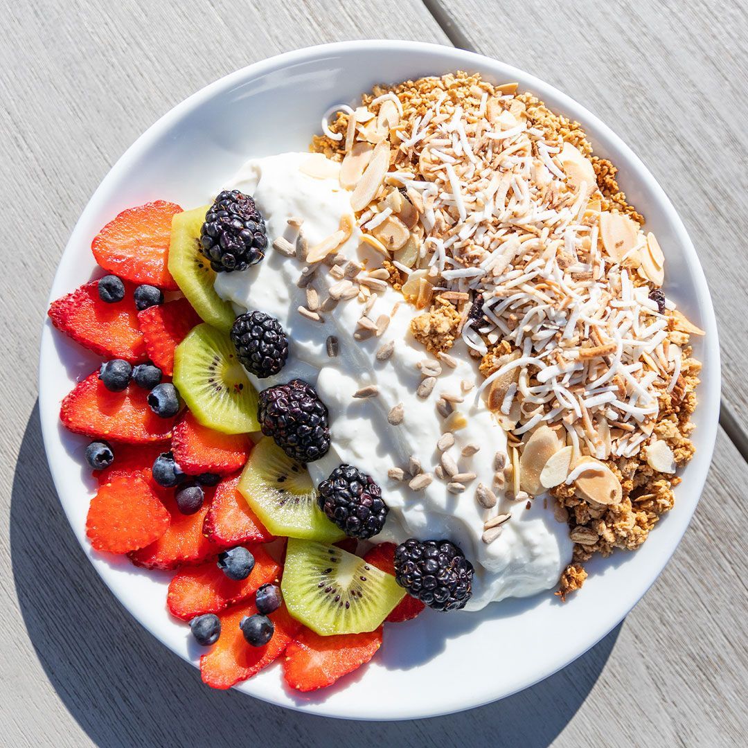 Bowl of yogurt, granola, and fruit: strawberries, kiwi, blueberries, blackberries, and sliced almonds.