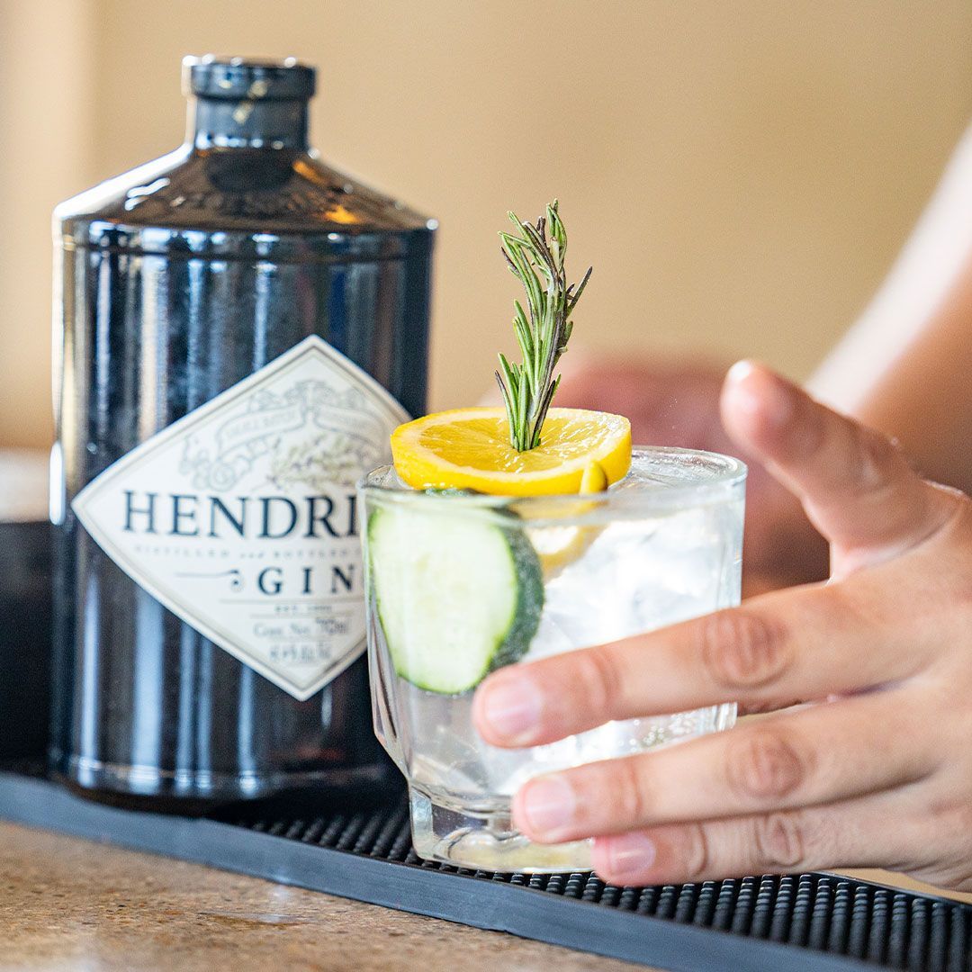 Hendrick's gin bottle next to a cocktail garnished with a cucumber, lemon, and rosemary.