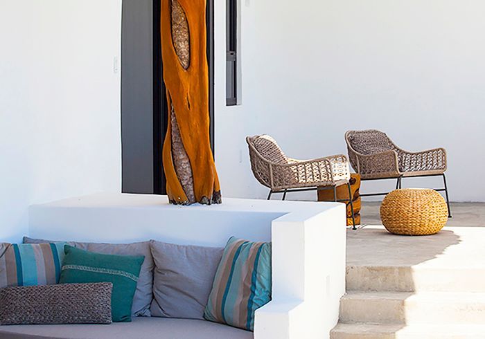 Outdoor seating area with woven chairs, built-in sofa with pillows, and a decorative wooden sculpture.