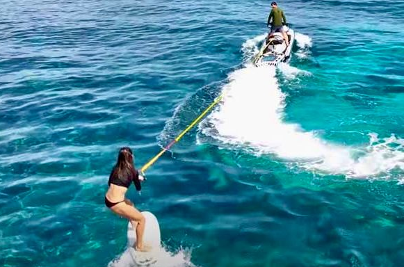 Beach scene with mountains, blue water, and birds on rocks.