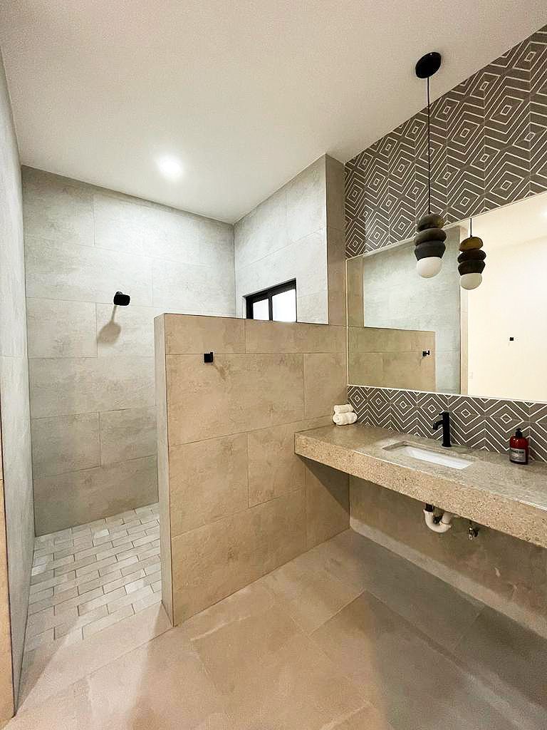 Modern bathroom with neutral tile, a walk-in shower, floating vanity, and decorative pendant lights.