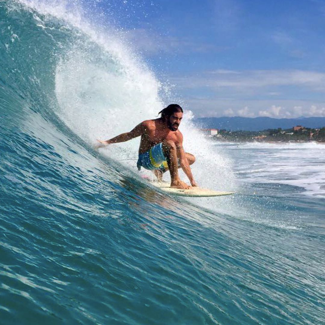 Man surfing inside a curling wave; bright blue ocean, sunny sky.