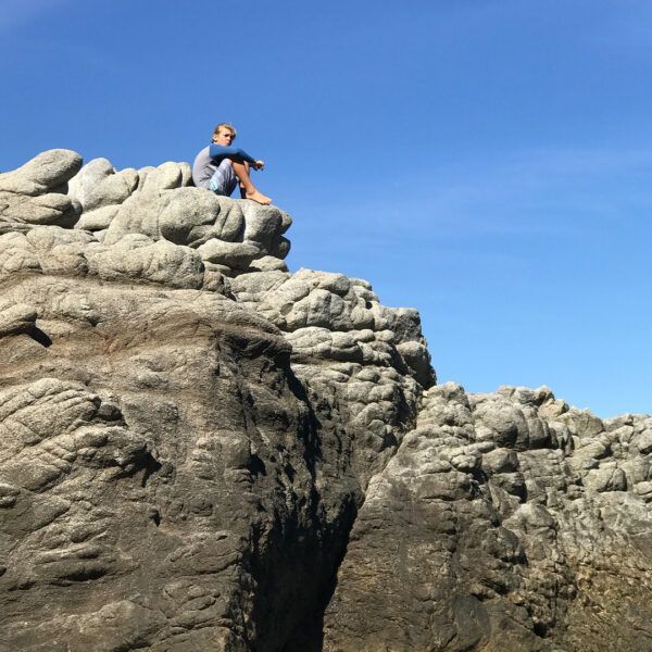 Person sitting on rocky outcrop, blue sky overhead.