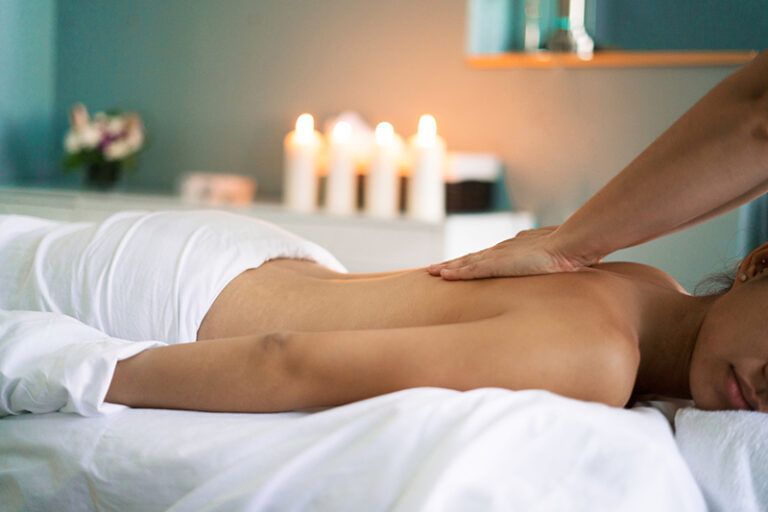 Person receiving back massage in a spa setting with candles and flowers.