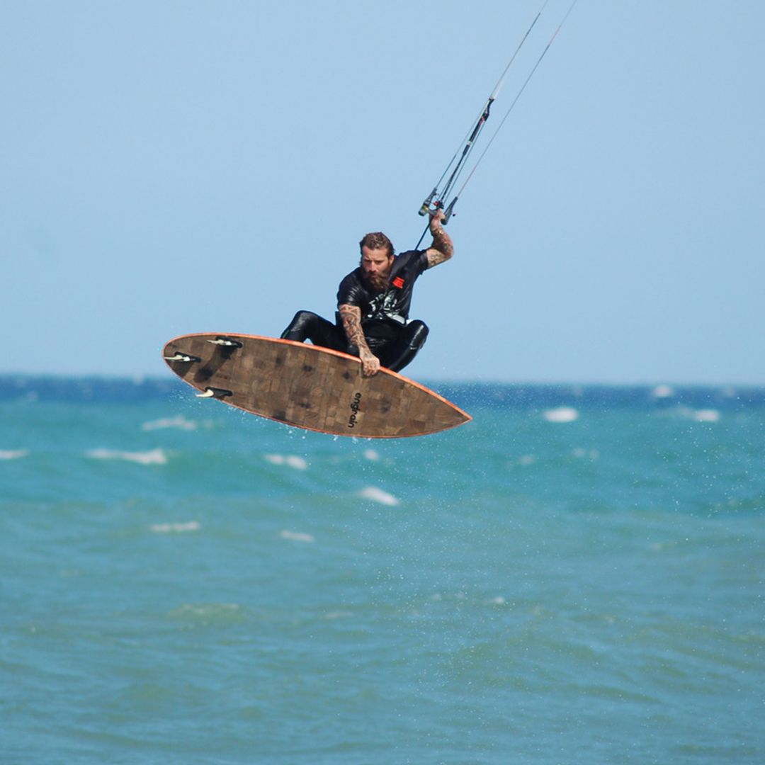 Kitesurfer airborne on a choppy ocean, board beneath him, kite overhead, against a blue sky.