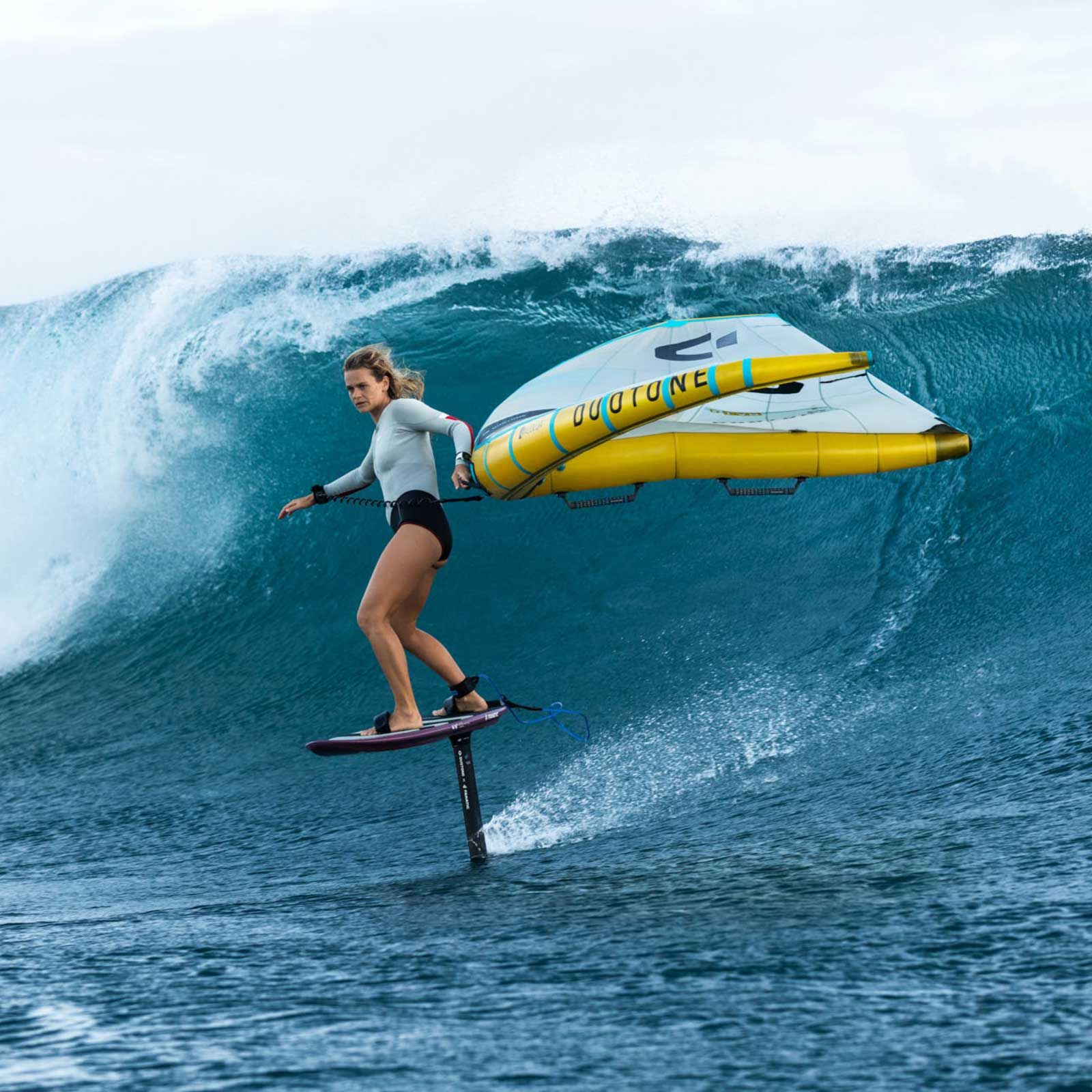 Woman wing foiling on ocean wave, with yellow wing and foil board.