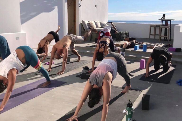 People doing yoga poses on a sunny rooftop overlooking the ocean.