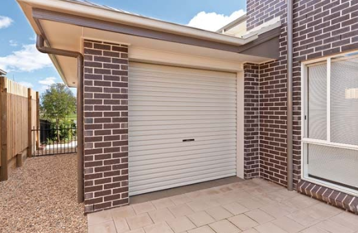 A brick house with a paved driveway leading to a white garage roller door.
