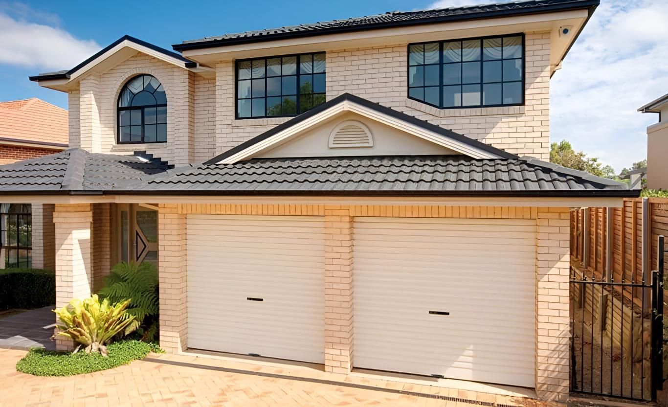 A Large Brick House With Two White Garage Doors And A Black Roof — Gold Coast Door Centre In Burleigh Heads, QLD