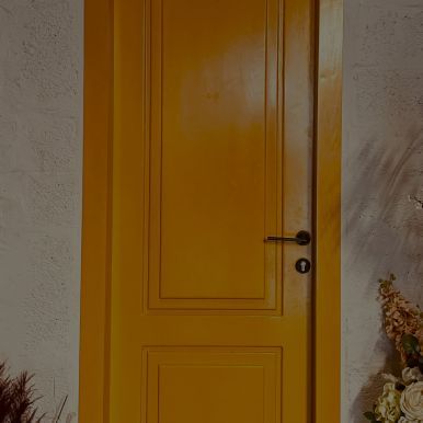 A yellow door is sitting on a white wall next to a vase of flowers.