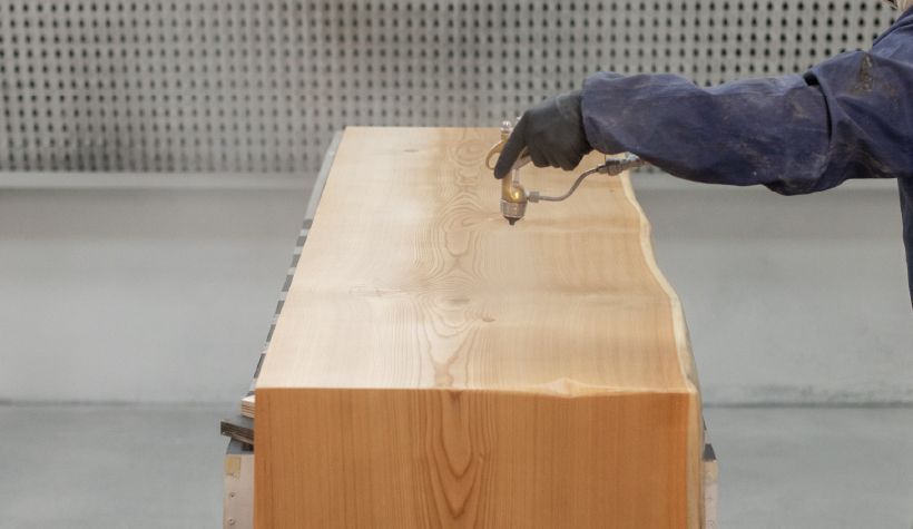 A person is painting a piece of wood in a workshop.