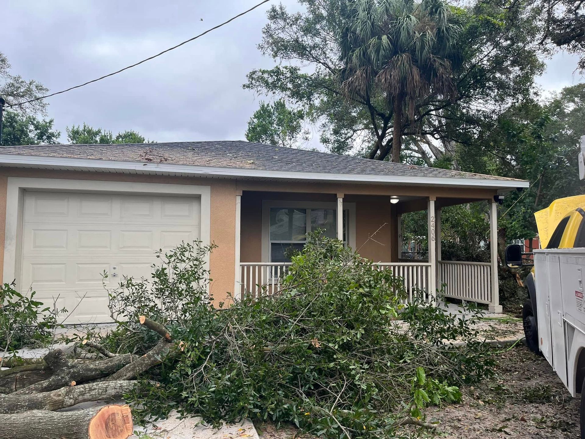 Single-story house with storm damage, fallen tree branches, and a truck in the driveway