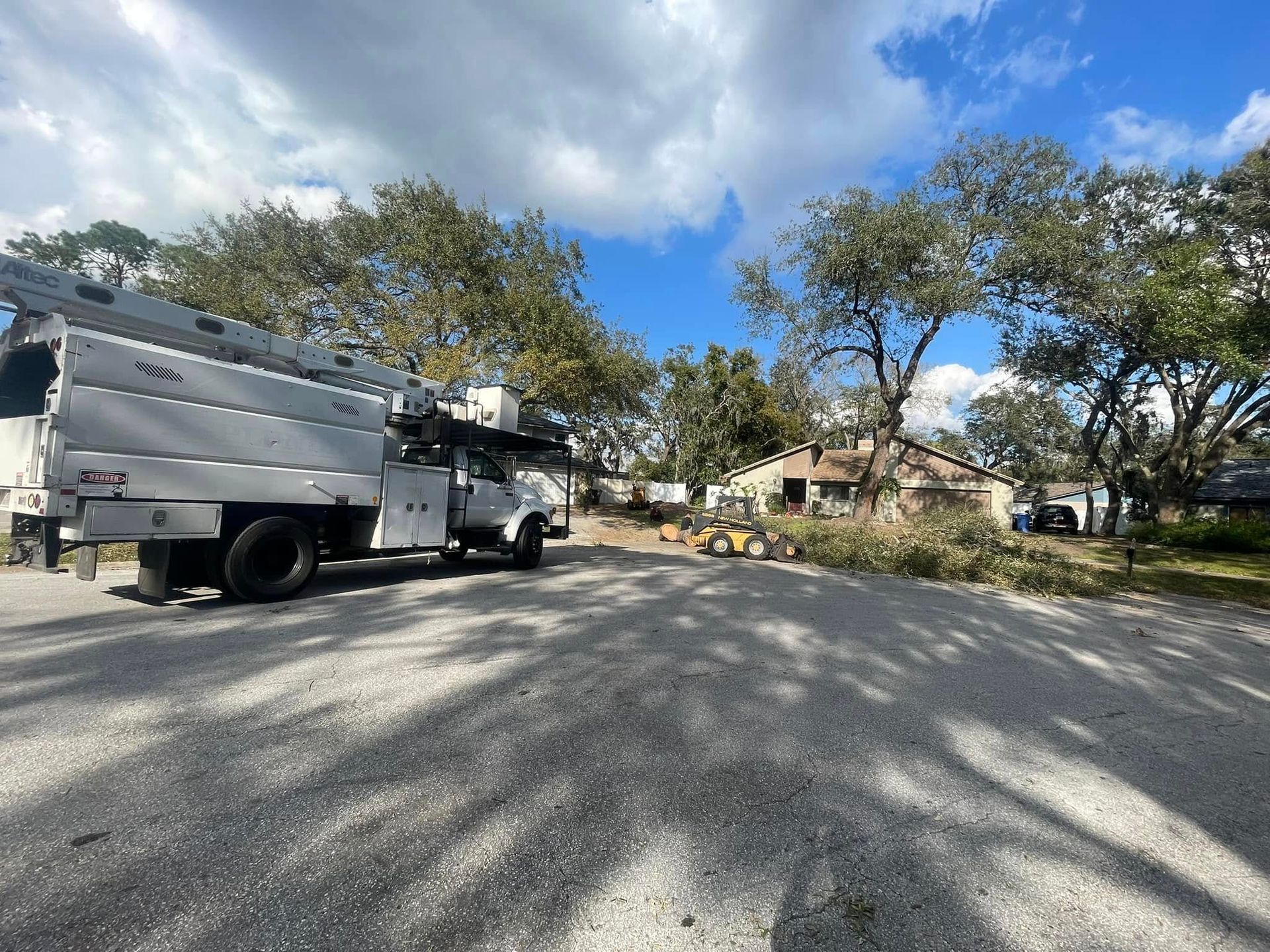 White utility truck parked on a tree-lined residential street under a partly cloudy sky