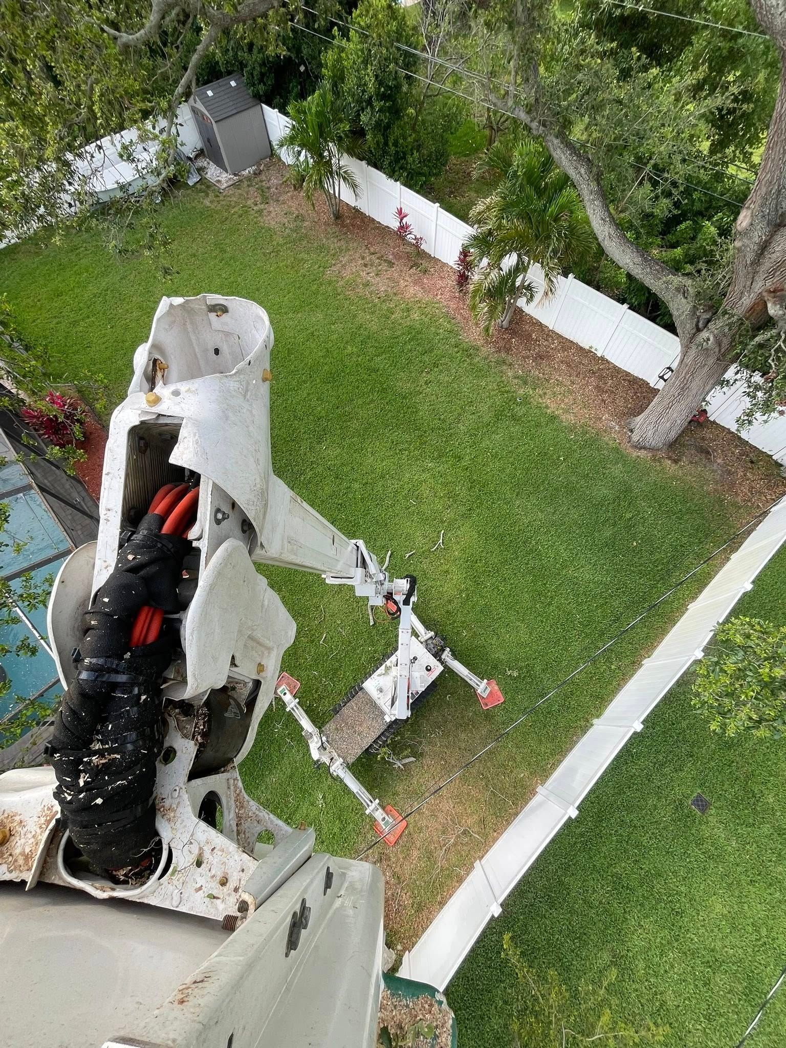High-angle view from a white tower onto a green yard with trees, fence, and a black cable/device in the foreground