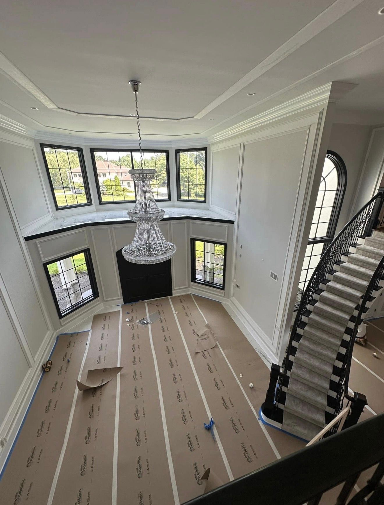 High-angle view of a large, two-story room with a grand staircase and a crystal chandelier.