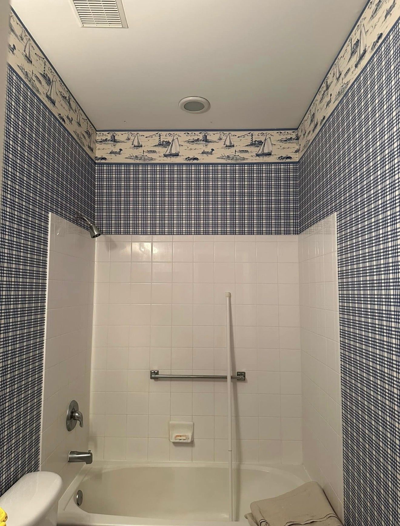 Bathroom with white tub and tile, blue plaid and wave patterned wallpaper.