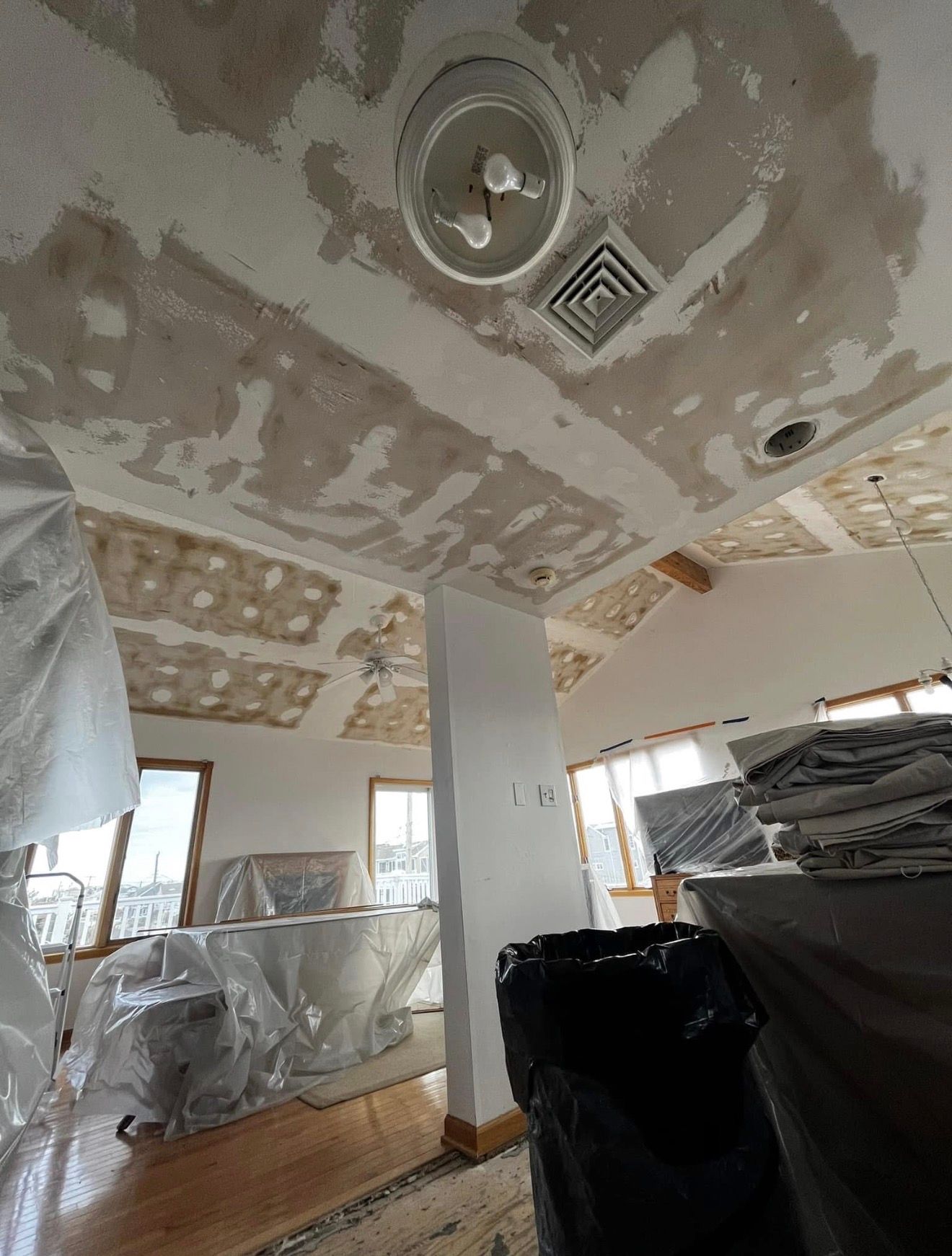 Ceiling under construction, showing drywall, light fixture, air vent, and covered furniture.