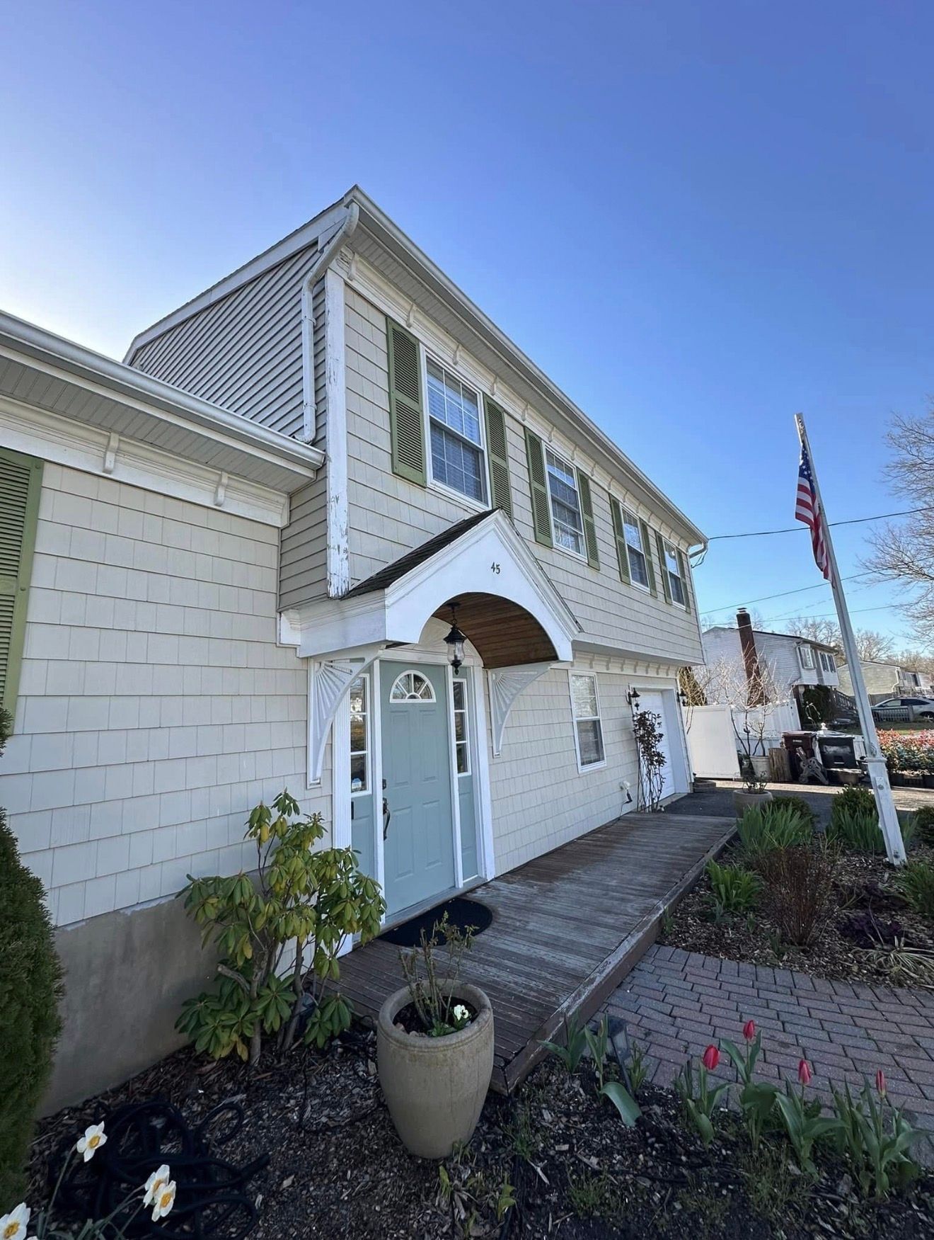 Two-story beige building with green shutters, awning, and American flag on a sunny day.