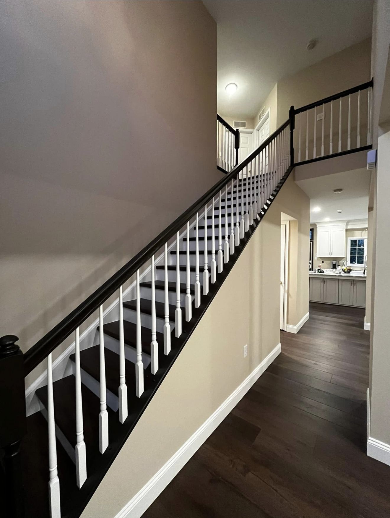 Staircase with black banister, white spindles, leading upstairs. Dark wood floors and neutral walls.