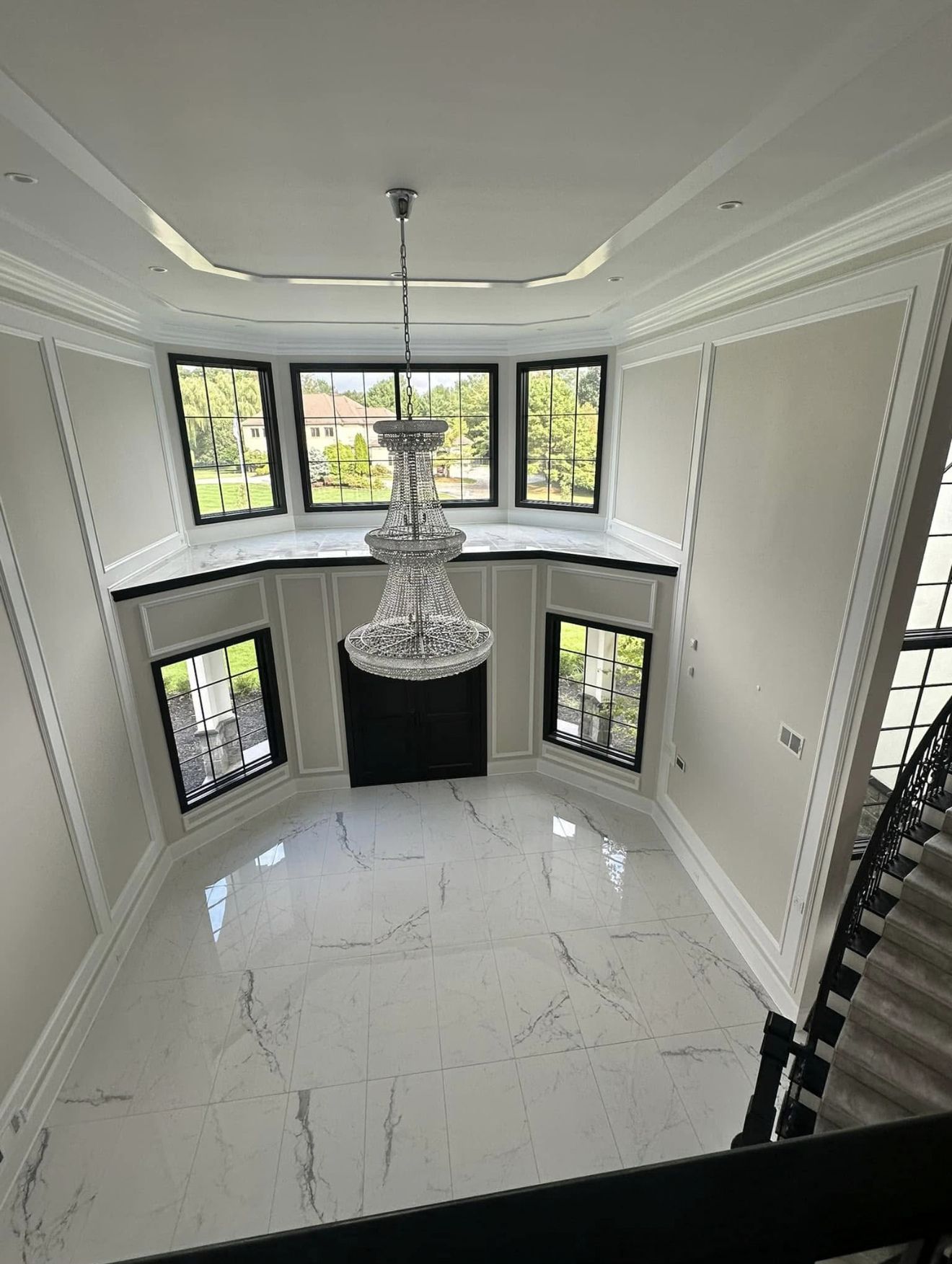 High-angle view of a luxurious foyer with white marble floor, ornate trim, windows, and a crystal chandelier.