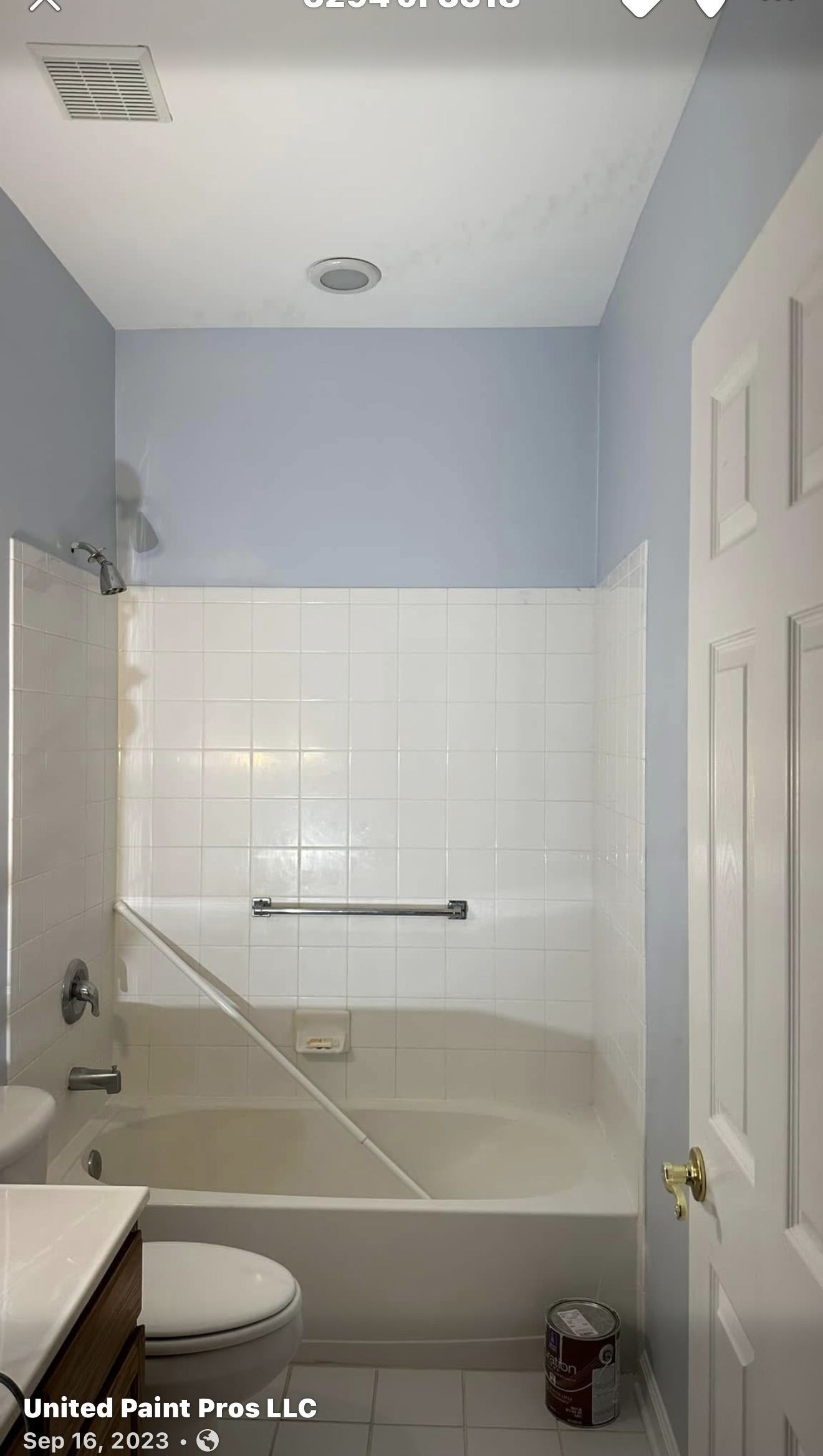 Bathroom with a white tub, toilet, and door; light blue walls and ceiling.