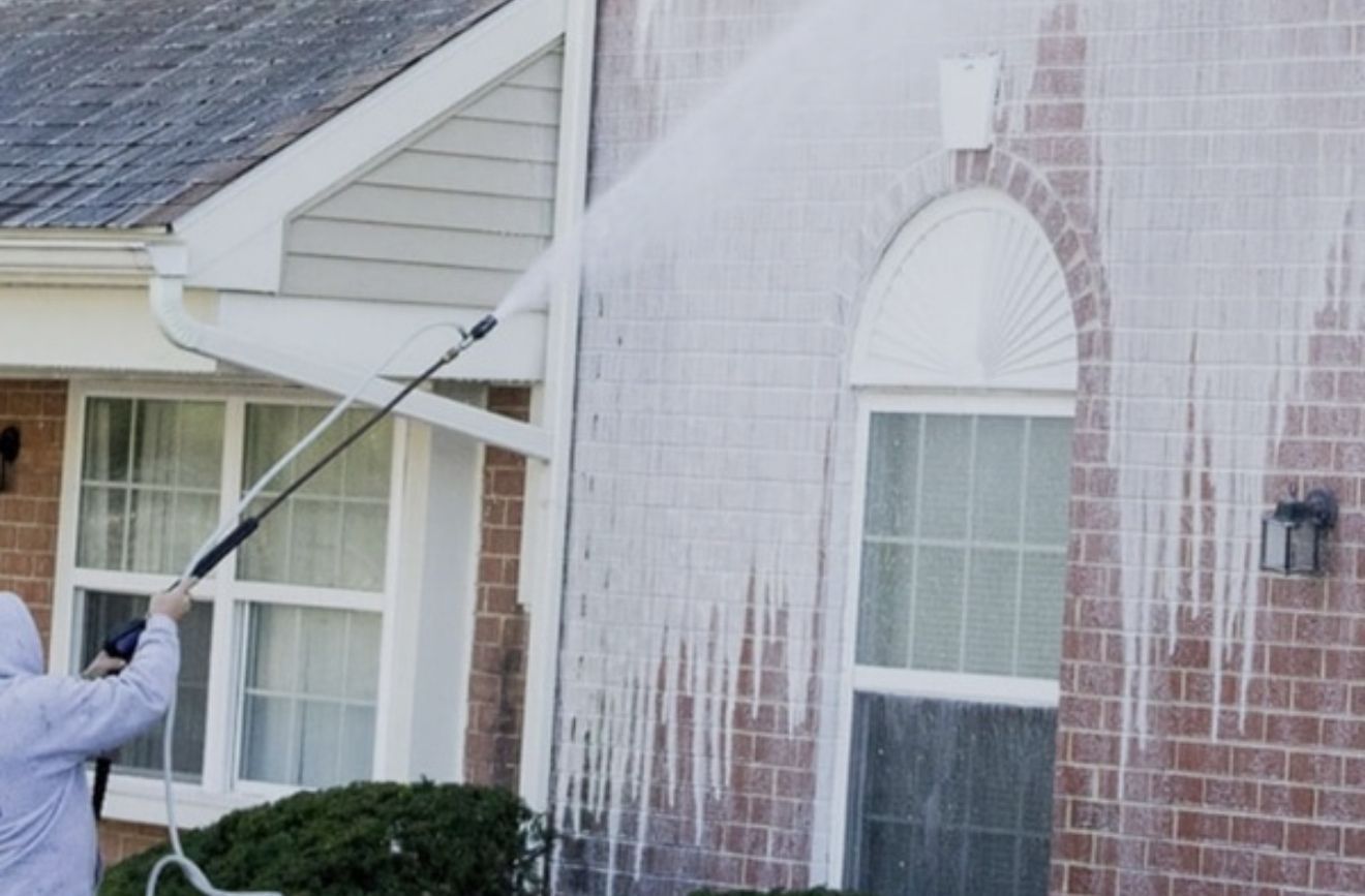 Person pressure washing the brick exterior of a house, water streaming down.