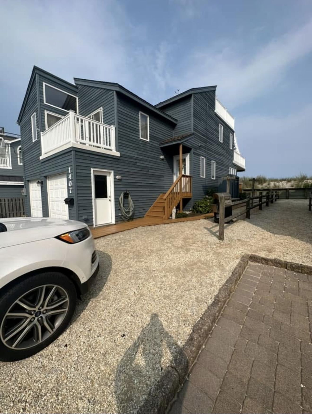 Dark blue beach house with white accents, parked car, and gravel driveway.