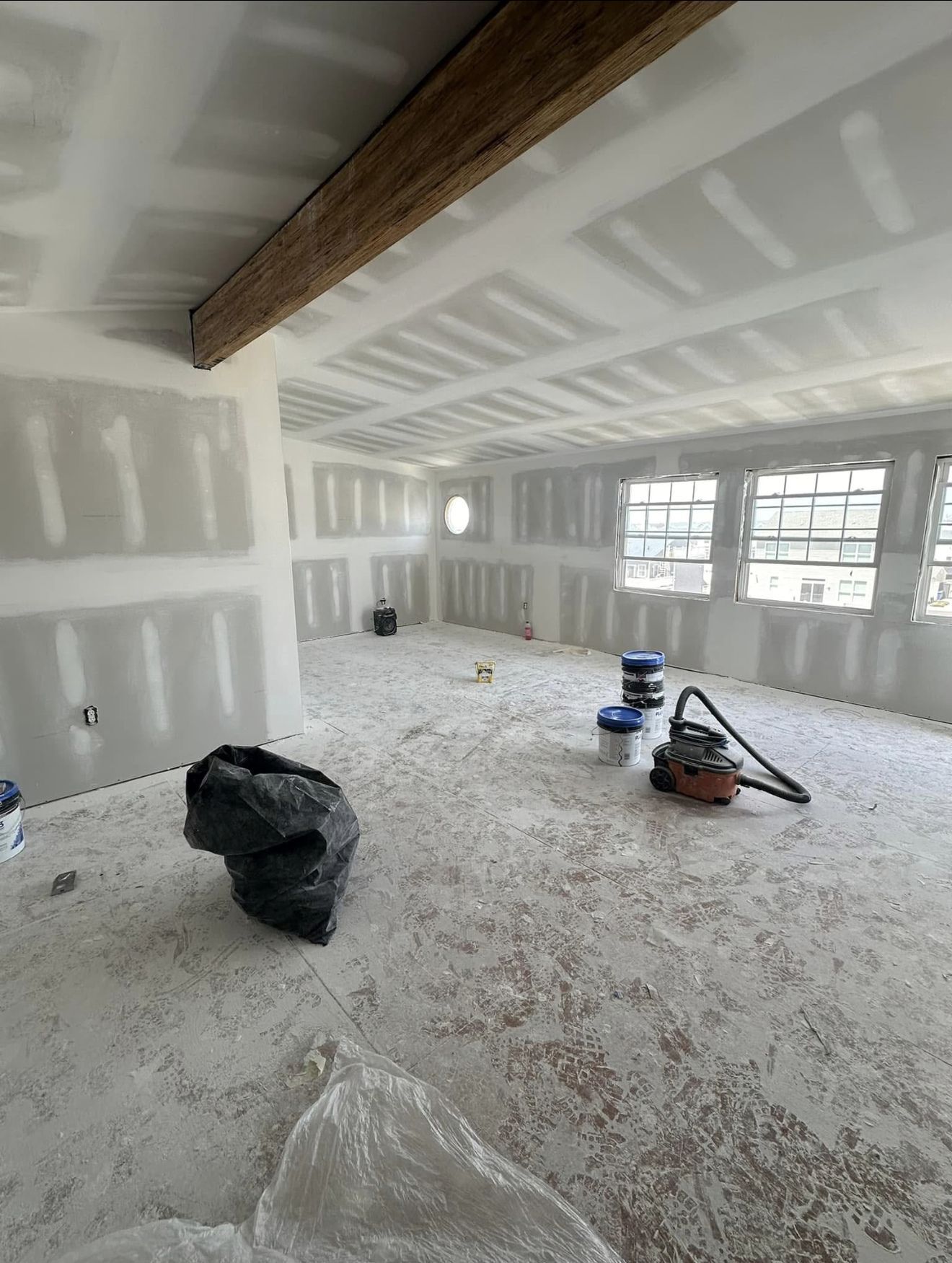 Interior of a room under construction with drywall and exposed ceiling beams. Debris covers the floor.