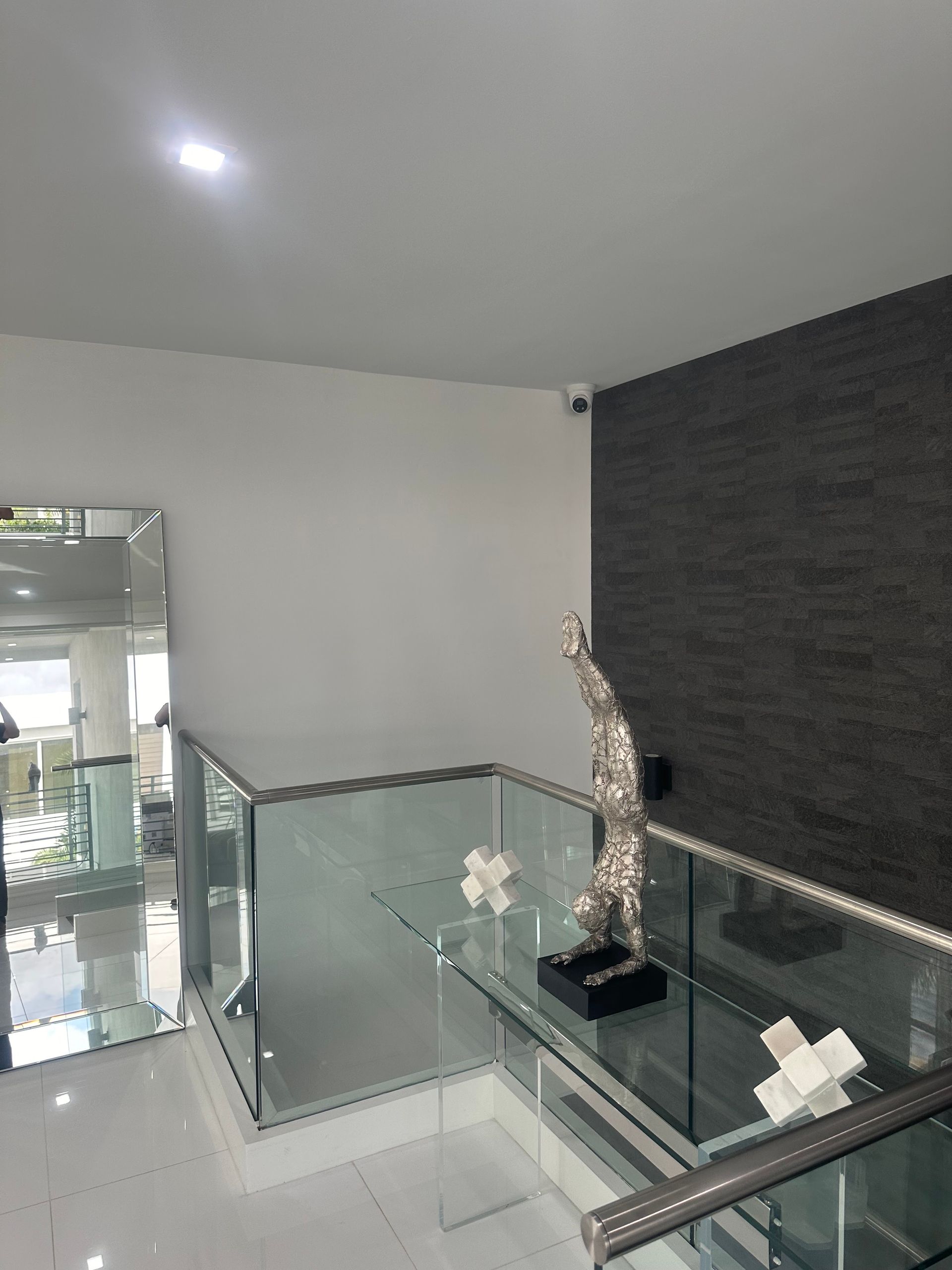 Modern hallway with glass railings and decorative sculpture. White walls and marble floors.