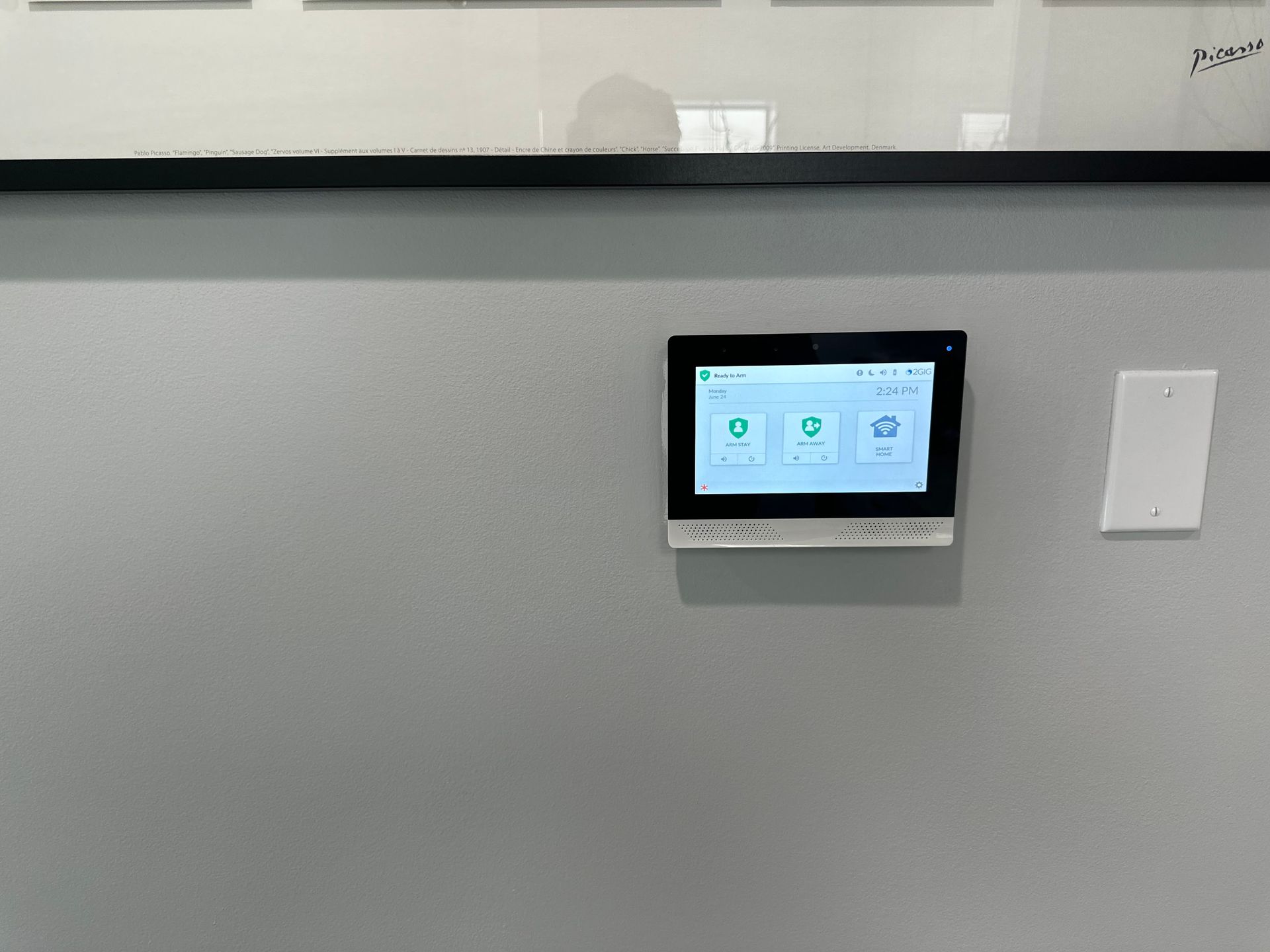 Gray wall with a mounted digital screen showing icons; next to it is a light switch.