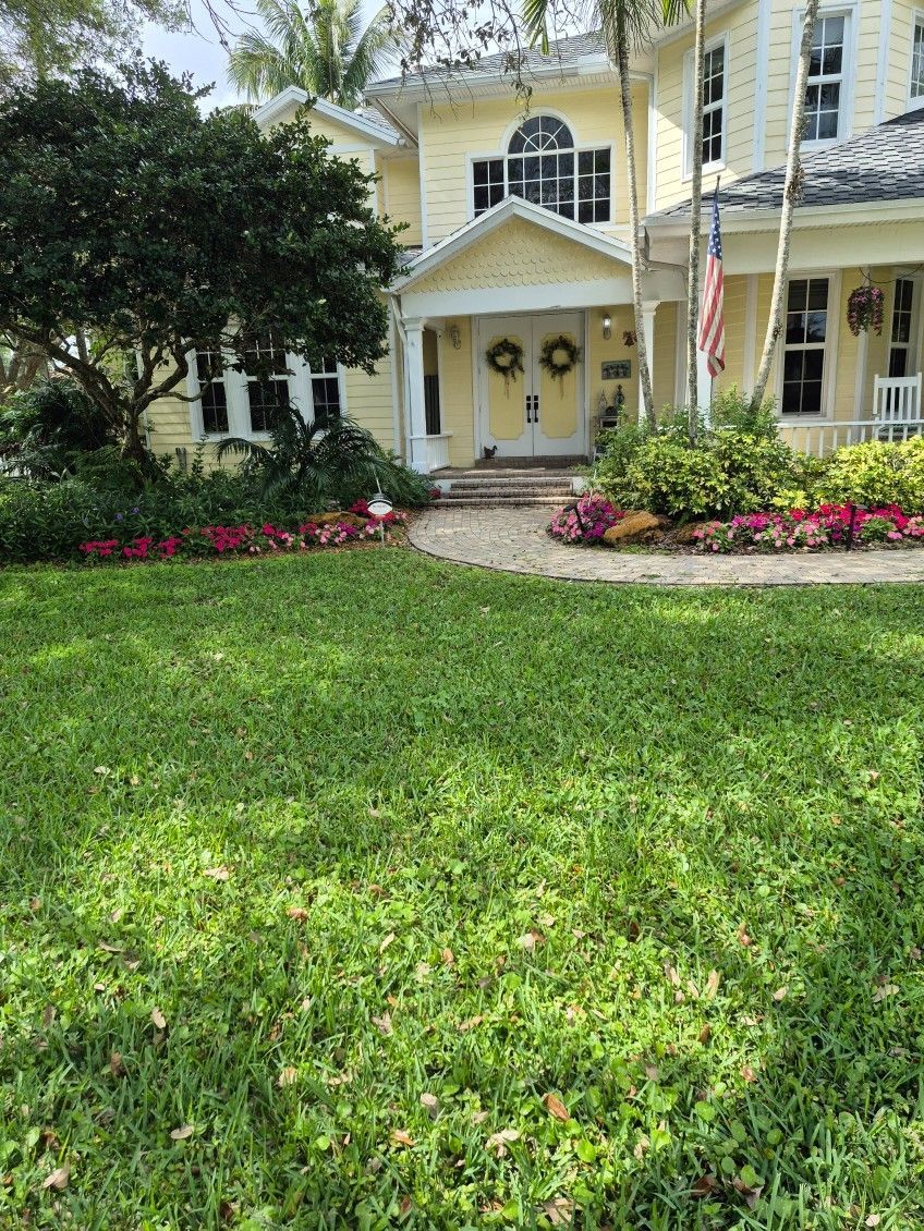 Yellow house with green lawn, flowerbeds, and a walkway leading to the front door.